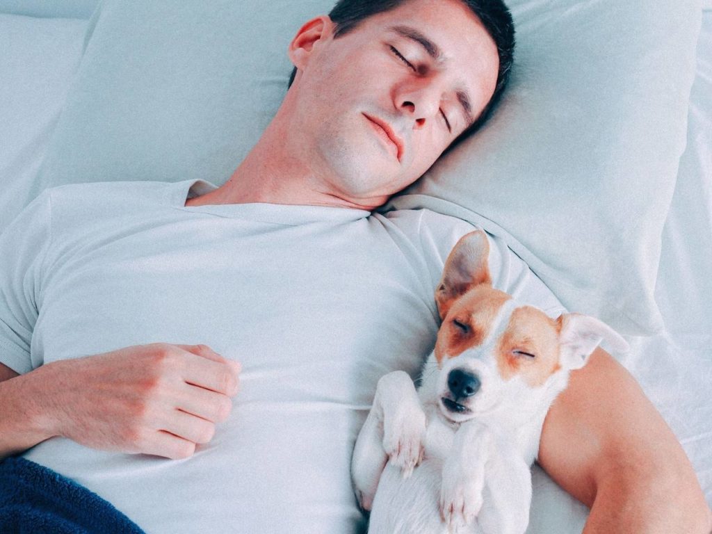 homem dormindo relaxadamente com um cachorro em seus braços