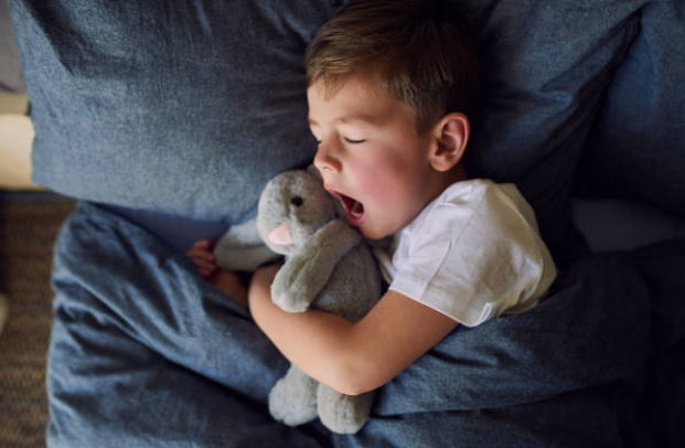 criança deitada abraçada com ursinho bocenjando