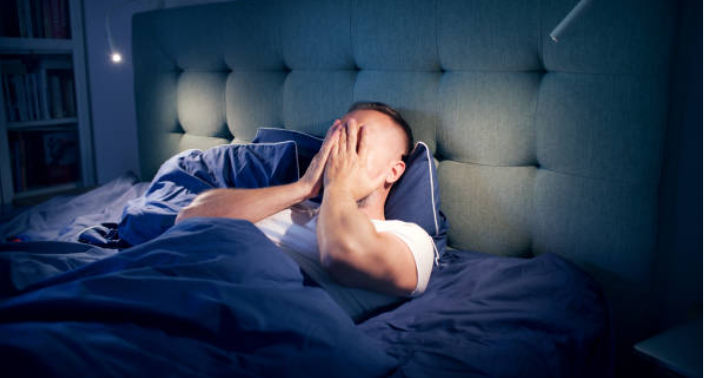 homem jovem deitado na cama com as mãos cobrindo o rosto