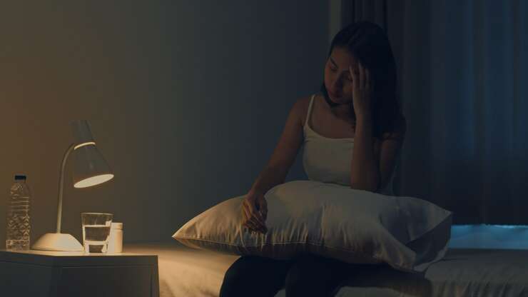 Mulher sentada na cama, parecendo pensativa à noite.