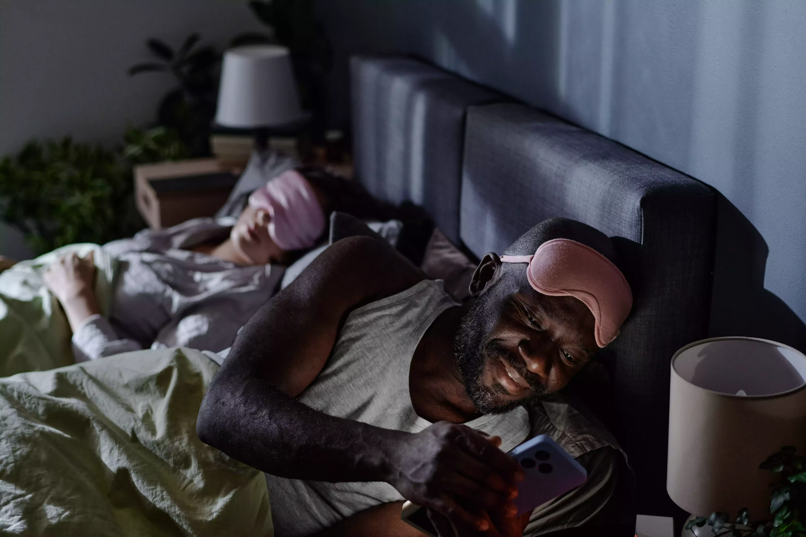 mantextingonsocialnetwork20250211052143utc Homem deitado na cama ao lado de uma mulher dormindo enquanto ele mexe no celular