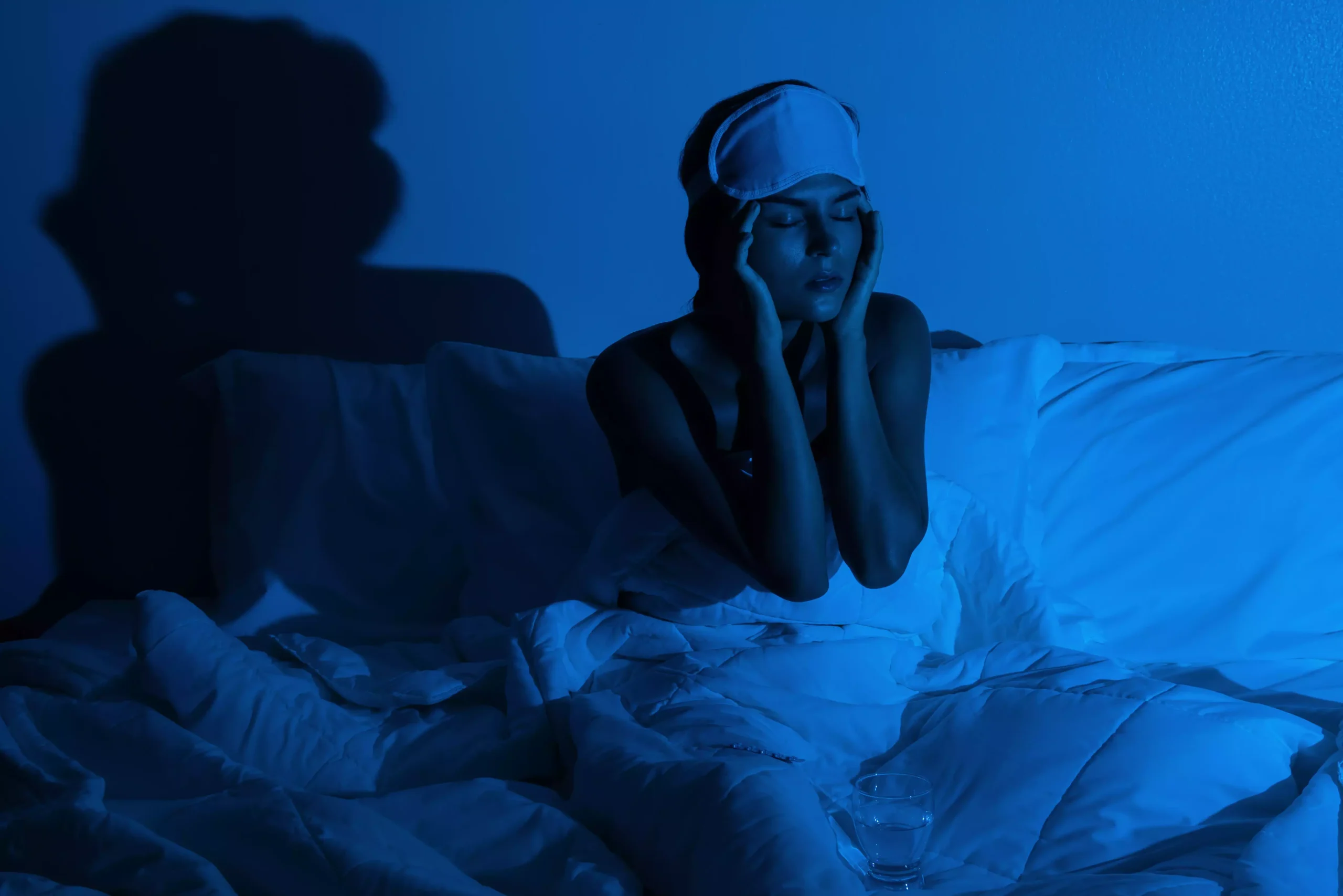 Mulher sentada na cama a noite sem conseguir dormir