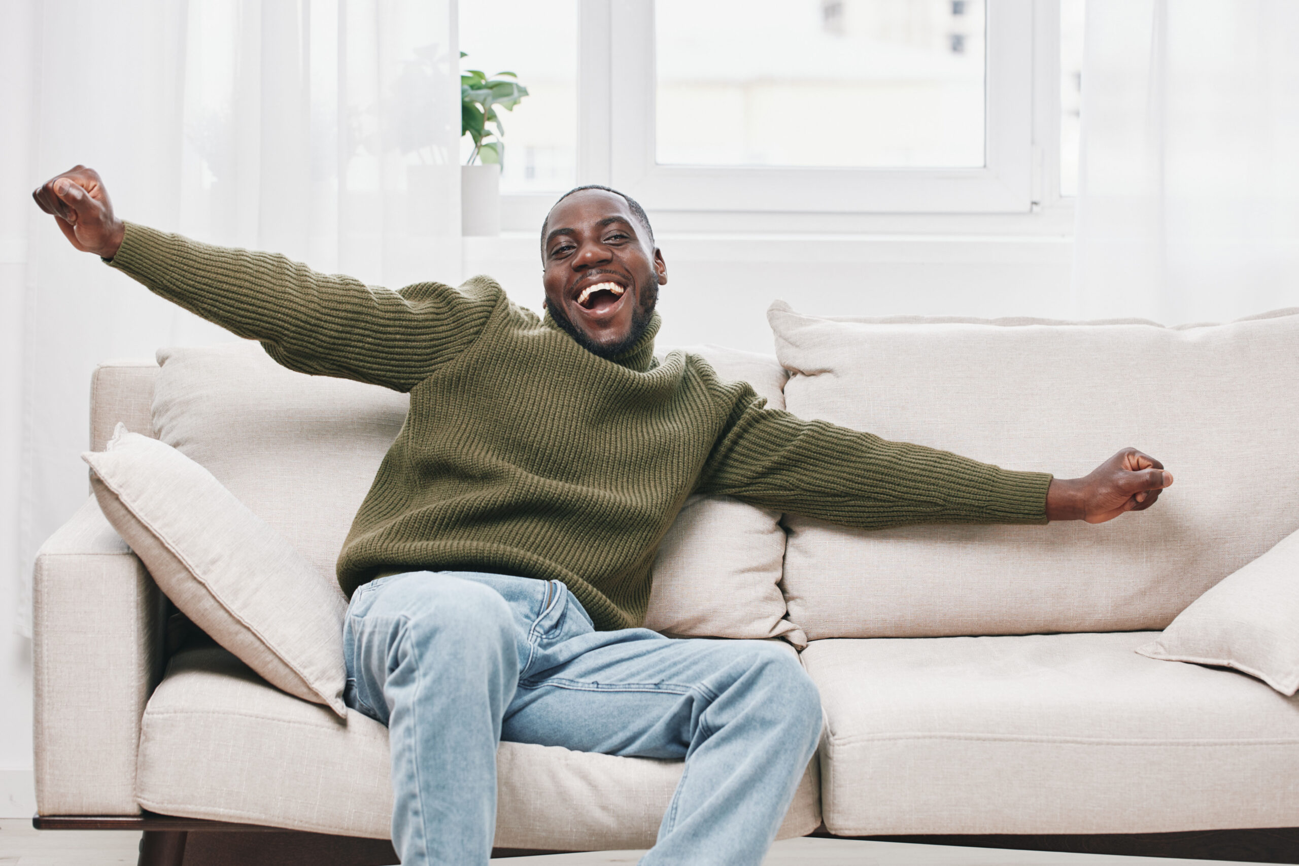 Homem sentado no sofa com braços abertos feliz