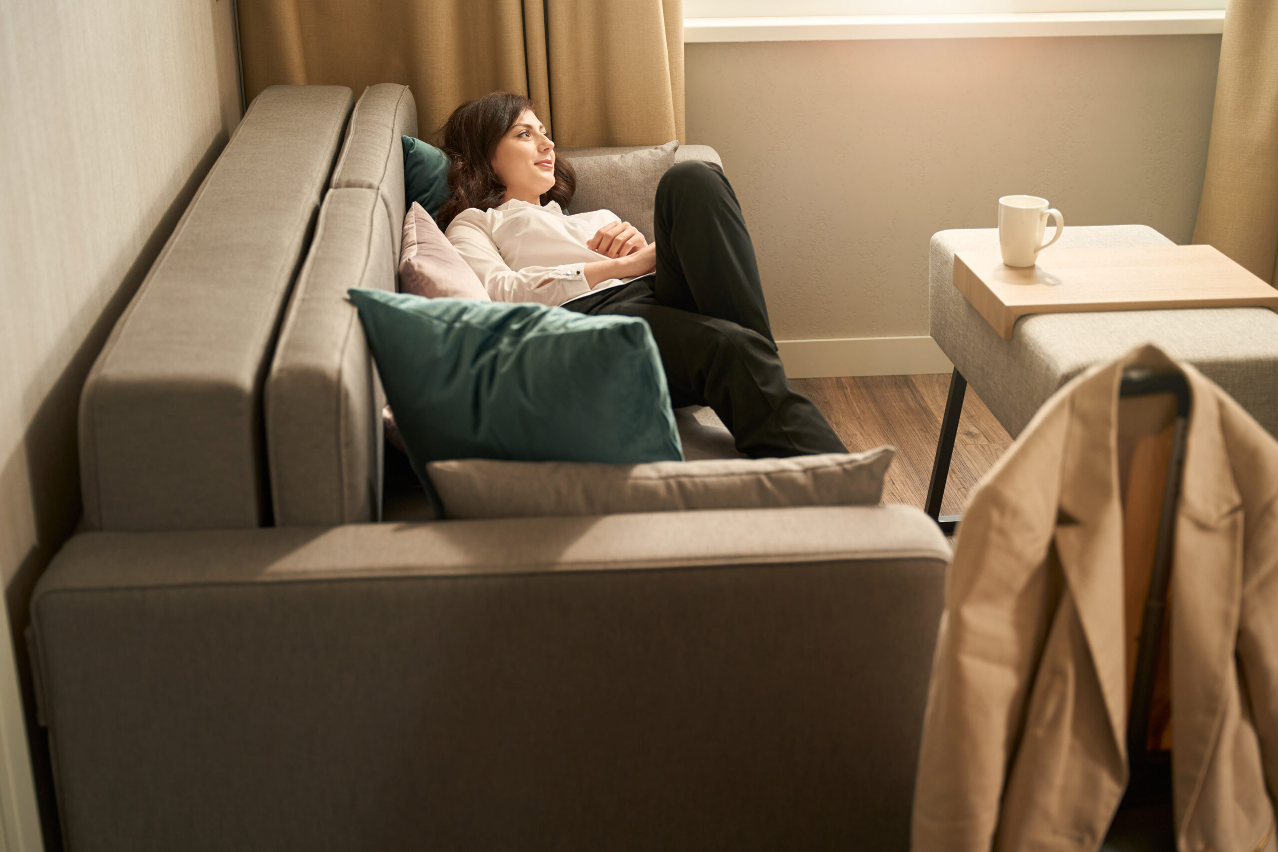 Satisfied young woman is located on sofa in hotel room Mulher deitada no sofa assistindo tv
