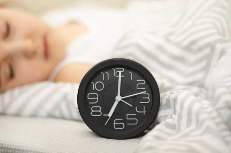 alarmclockonbedcutekidgirlsleepingonthe20241206033306utc Criança deitada dormindo com relógio na frente sendo focado.
