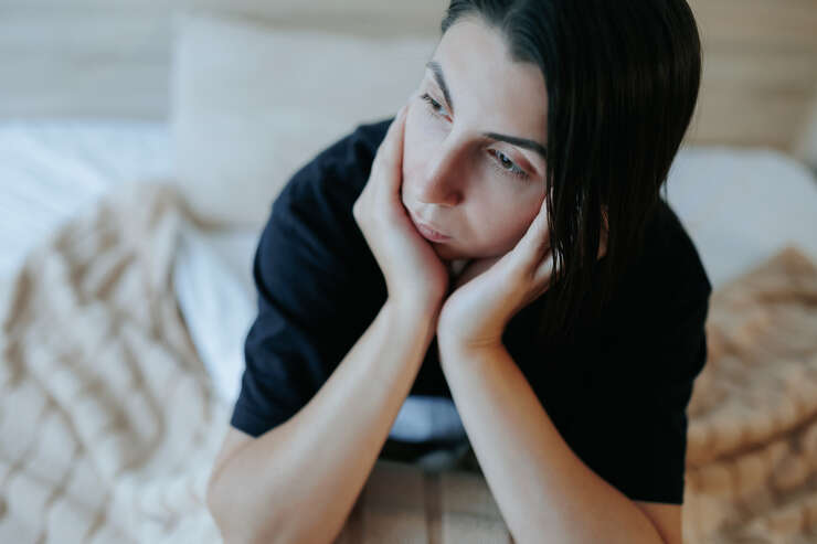 Mulher deitada na cama com as maos no queixo