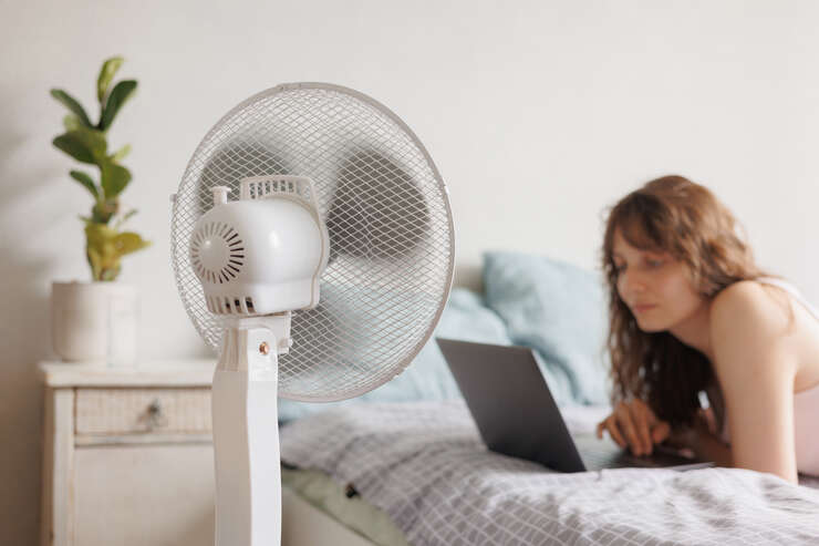 mulher mexendo no notebook com ventilado ligado em sua direçao