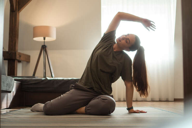 Mulher sentada no chão da sala se alongando