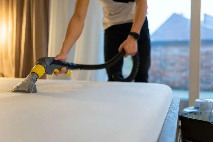 mattresscleaningprocessmancleansbedfromdir20241018082020utc Homem passando aspirador de po no colchao.