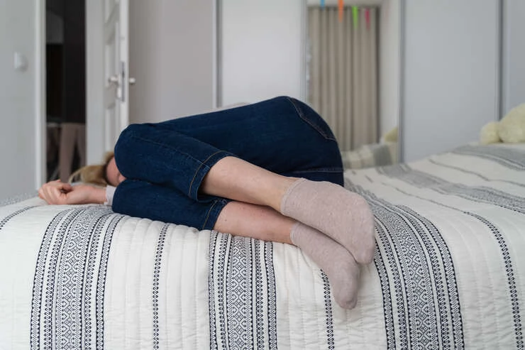 Mulher deitada na cama com as pernas encolhidas.