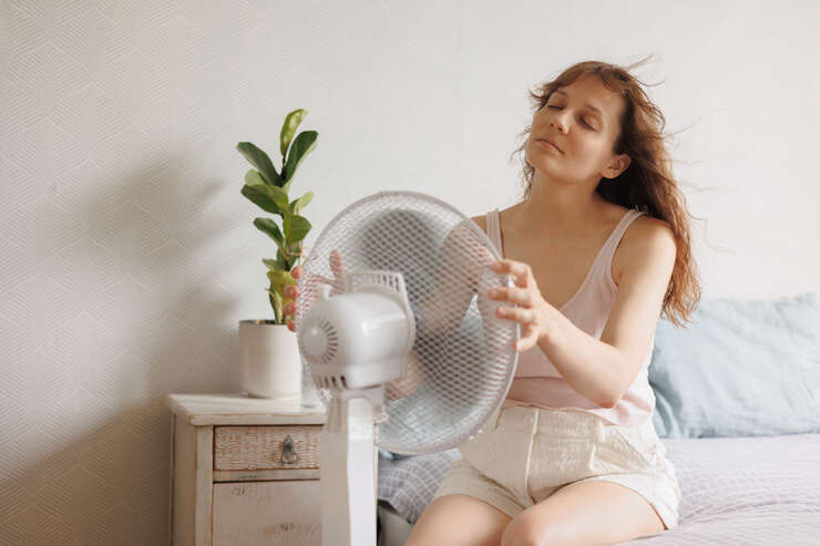 Mulher sentada na cama em frente ao ventilador
