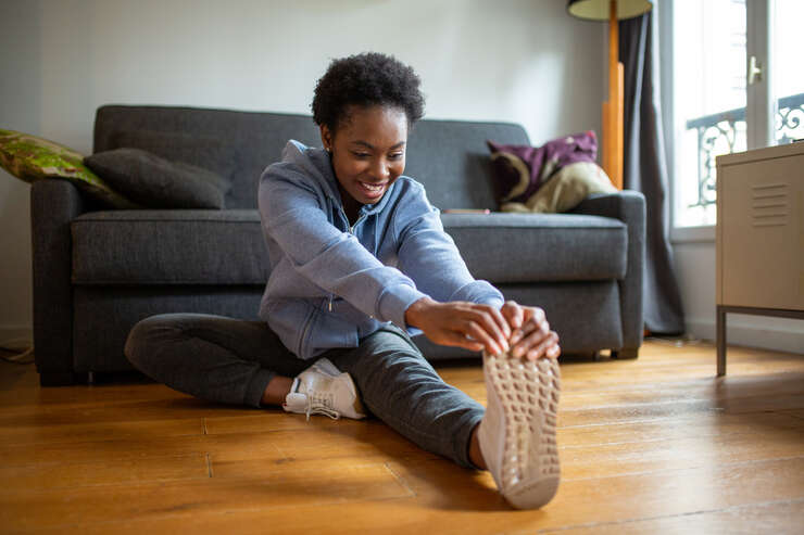 Mulher sentada no chão da sala se alongando