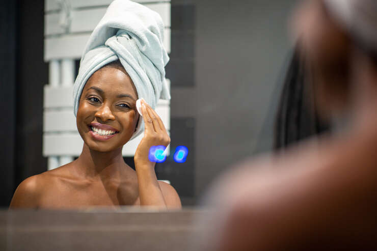 Mulher olhando para o espelho sorrindo com toalha na cabeça