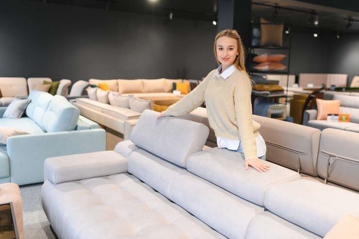 Mulher branca apoiada em sofa na cor bege