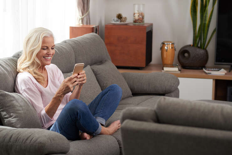 Mulher sorridente usando celular no sofá