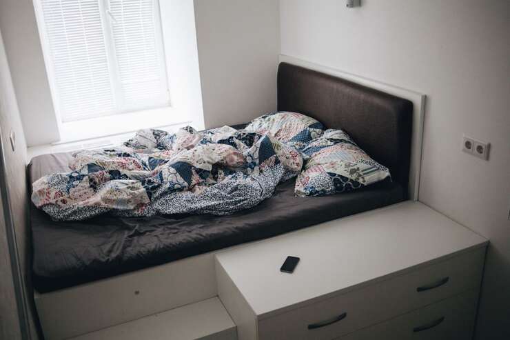 Cama desfeita com roupas de cama coloridas em quarto moderno